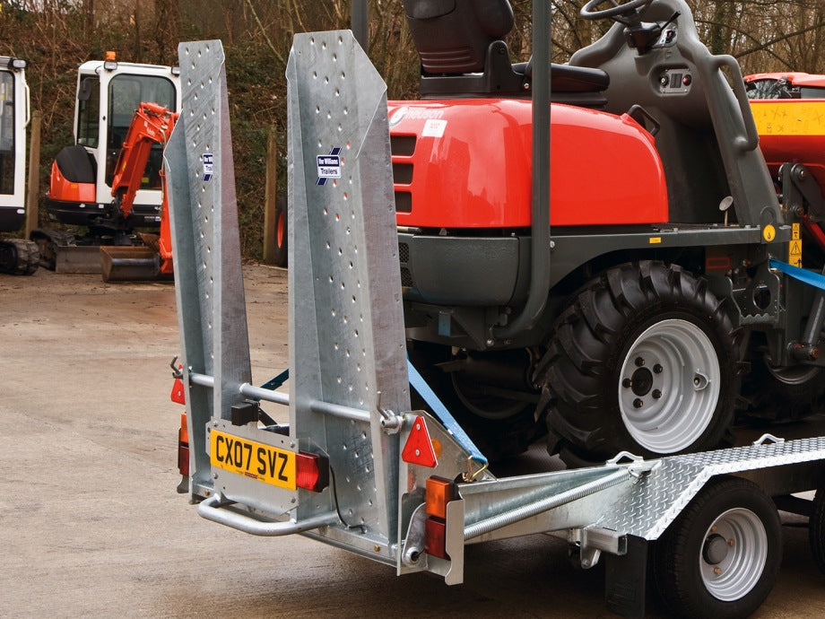 Red tractor on a trailer with a license plate, surrounded by other equipment in an outdoor setting.