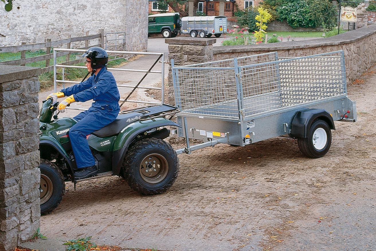 Person operating a green ATV with a trailer attached, parked on a stone path.